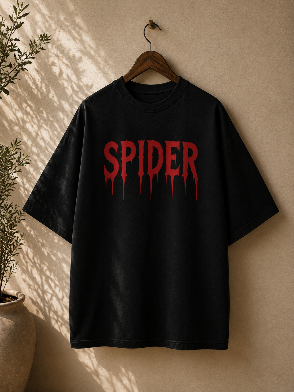 A black oversized short-sleeve t-shirt hanging on a wooden hanger against a textured beige wall, featuring a bold red dripping 'SPIDER' graphic on the chest.